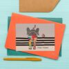 Die lustige Postkarte zeigt den bunt gemusterten Dickhäuter von hinten, der fröhlich mit erhobenen Rüssel seinen Weg geht und ein „Be Happy“ vor sich her trötet. Mit Liebe designed von der Regensburger Künstlerin Sabine Leipold.